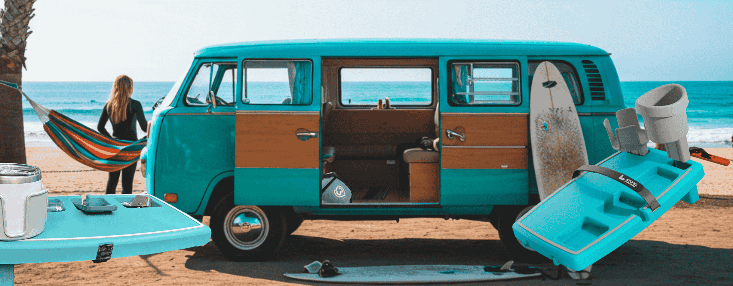 Teal and brown vintage van on a beach with surfboard and equipment.